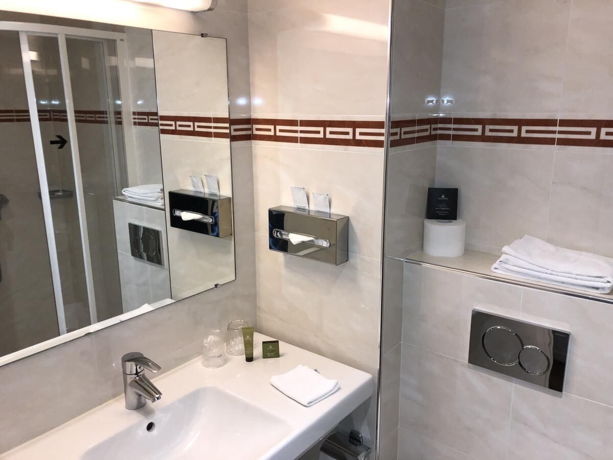 A modern bathroom with a sink, mirror, towel dispenser, and glass shower enclosure.