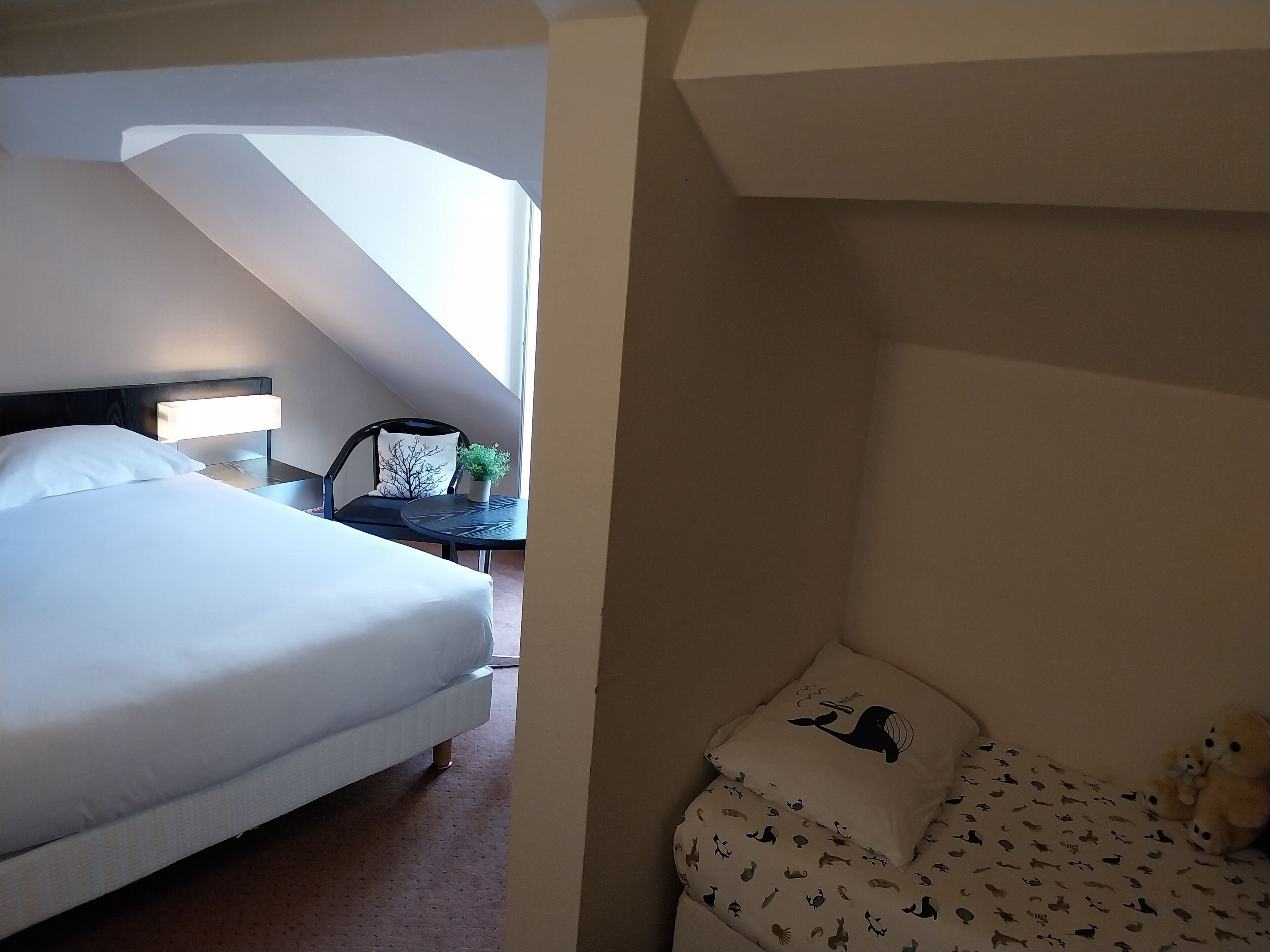 A bedroom with a bed, a nightstand, a chair, and a small table with a plant.