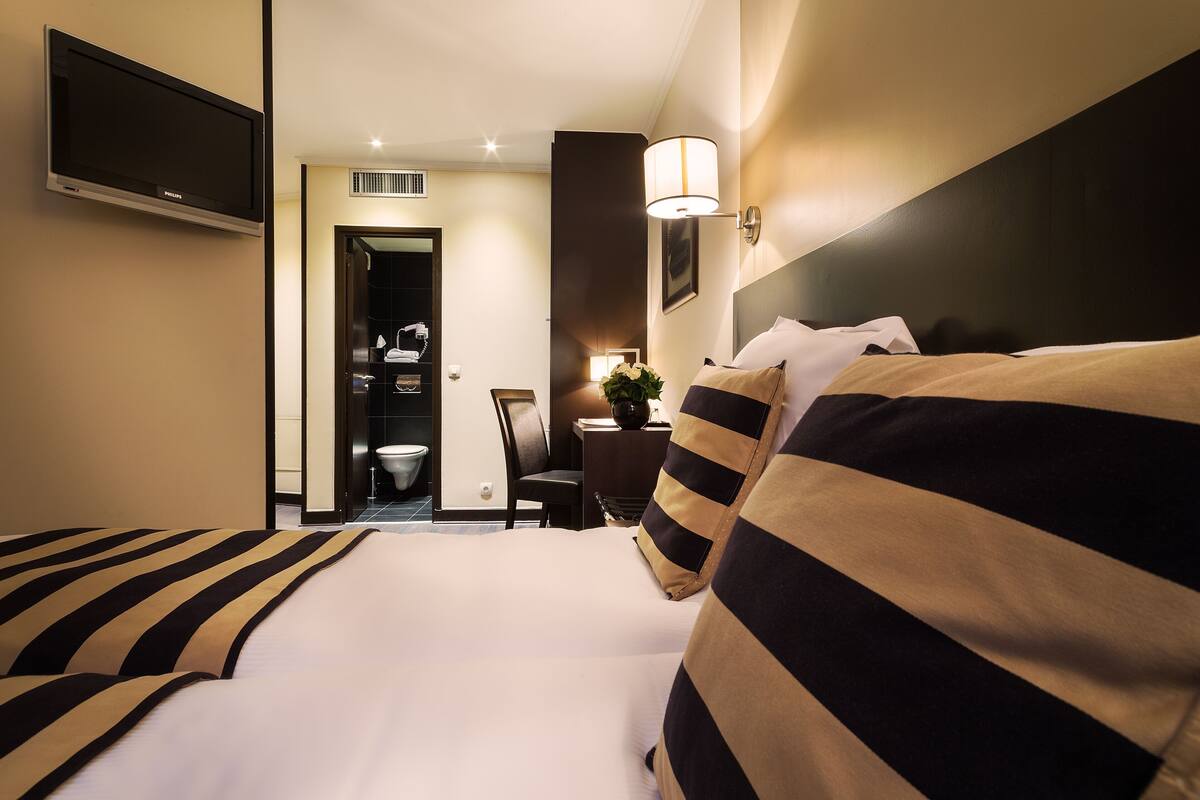 Habitación de hotel con cama, televisor, escritorio con silla y baño visible a través de una puerta abierta.