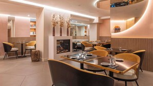 A modern restaurant with round tables, comfortable chairs, and a central fireplace. - Hotel Arc Elysees (Paris)