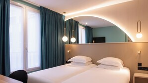 A hotel room with two beds, a desk, and a chair. There is a window with curtains, a mirror, and a wall-mounted TV. - Hotel Arc Elysees (Paris)