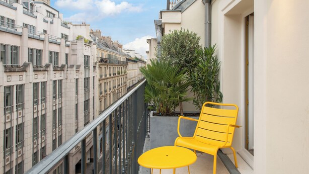 A balcony with a yellow chair and a small table, overlooking a row of buildings. - Hotel Arc Elysees (Paris)