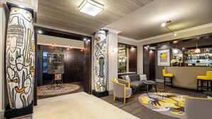 A modern lobby with a bar area, featuring a unique art installation on the pillars, a seating area with a patterned rug, and a bar stocked with various bottles. - Hôtel Le Marquis by Inwood Hotels (Paris)