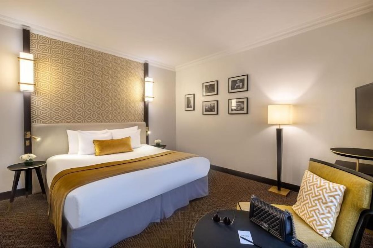 A hotel room with a large bed, a bedside table, a lamp, and framed pictures on the wall.