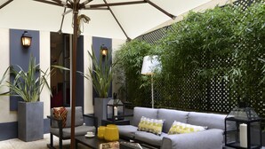 A modern outdoor seating area with a grey sofa, black tables, and potted plants. - Hôtel Le Marquis by Inwood Hotels (Paris)
