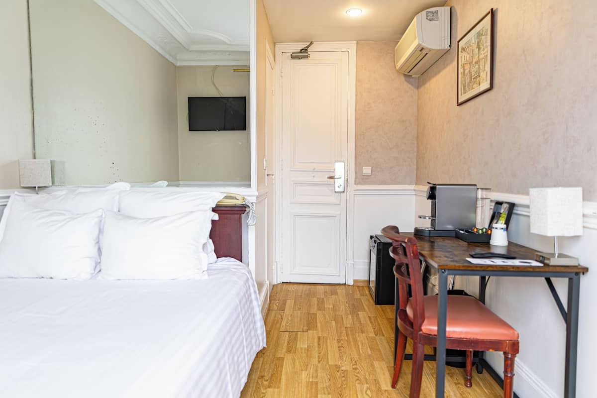 A hotel room with a bed, a desk, a chair, a television, and an air conditioner.