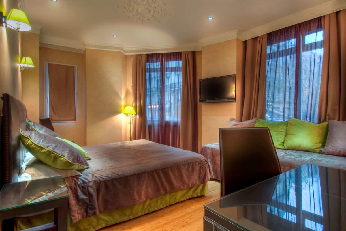 A hotel room with a bed, a desk, a chair, a TV, and large windows with curtains.