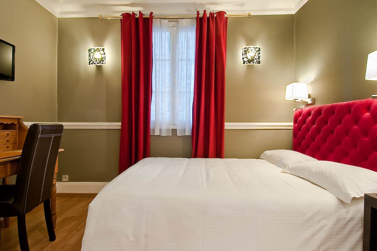 A hotel room with a bed, a desk, and two wall-mounted lamps.