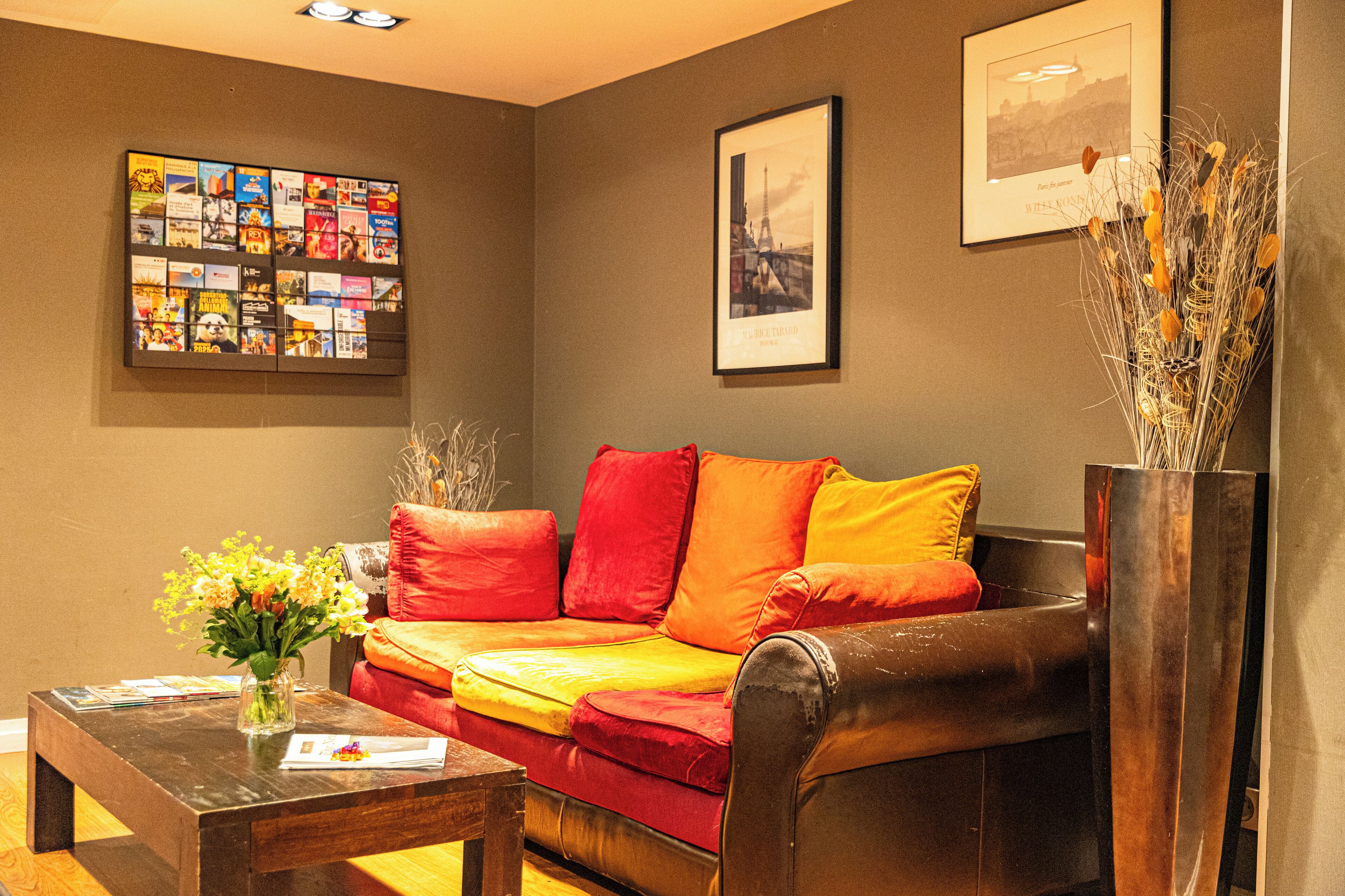 A living room with a red and yellow sofa, a coffee table with a vase of flowers, and a framed collage on the wall.