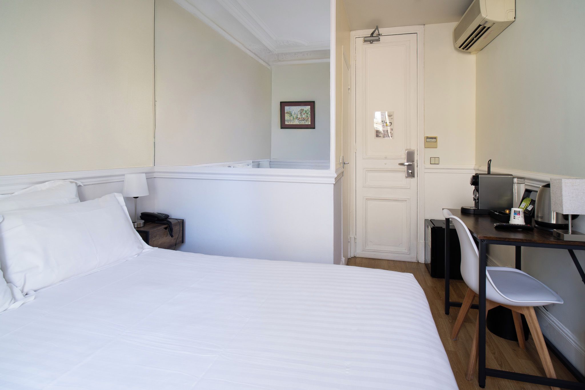 Habitación de hotel con cama, escritorio, silla, puerta y una mesita con tetera.