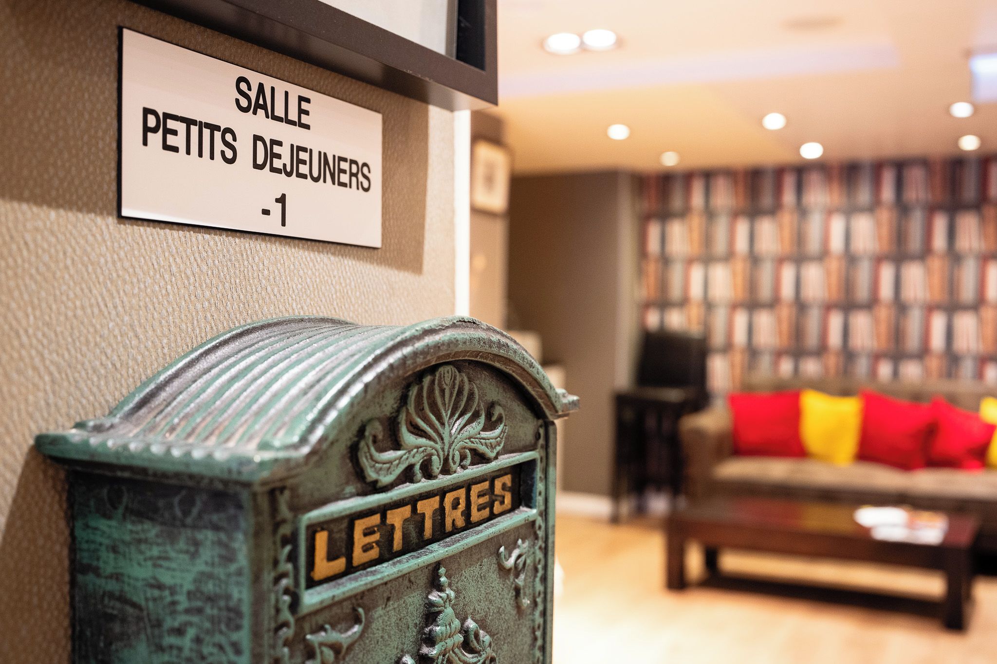 En ældgammel postkasse med ordet 'LETTRES' på, placeret i et rum med en bogreol og en sofa i baggrunden.