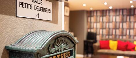 En ældgammel postkasse med ordet 'LETTRES' på, placeret i et rum med en bogreol og en sofa i baggrunden.