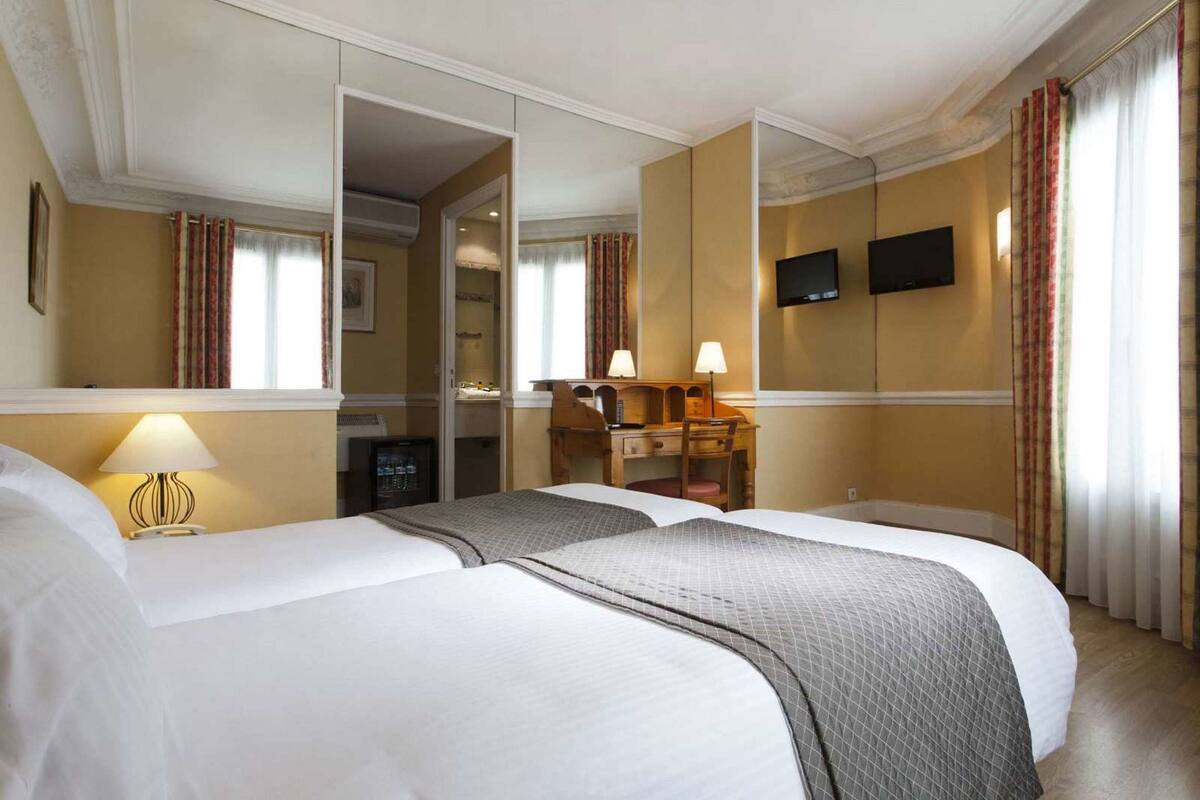 A hotel room with two beds, a desk, a chair, a television, and a mirror.
