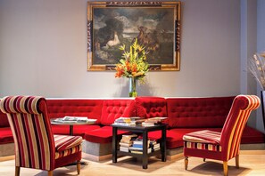 A red upholstered sofa set with striped armchairs, a small round table with books, and a vase of flowers on a stand. - Hotel Claude Bernard Saint Germain (Paris)