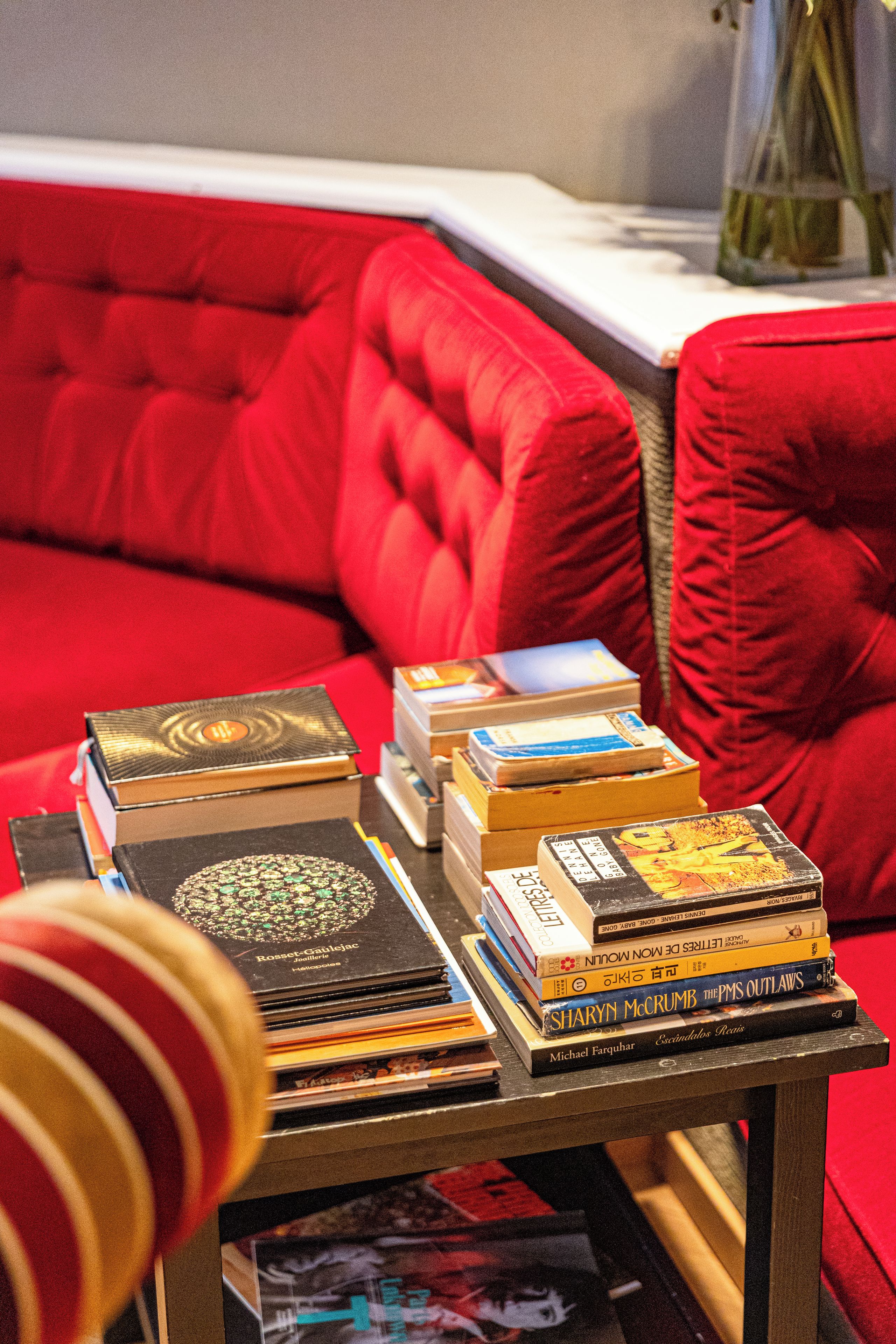 A stack of books on a table with a red couch in the background.
