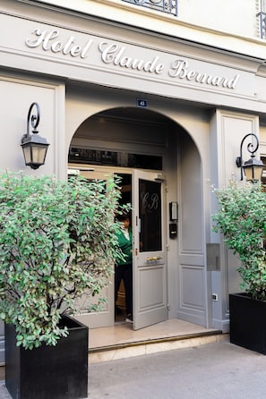 The entrance to Hotel Claude Bernard with a classic facade, an arched doorway, and two potted plants. - Hotel Claude Bernard Saint Germain (Paris)