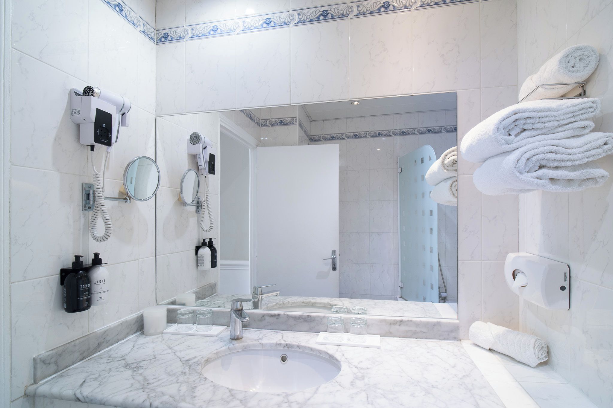 A modern bathroom with a marble sink, a hairdryer, a mirror, and a towel rack.