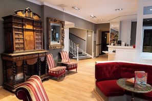 A modern living room with a grand wooden cabinet, striped armchairs, a red sofa, and a round table with books. - Hotel Claude Bernard Saint Germain (Paris)