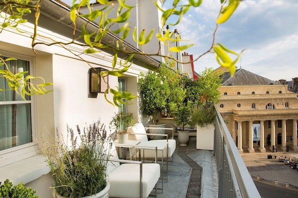 A balcony with white furniture, potted plants, and a view of a historic building. - Hôtel Baume (Paris)
