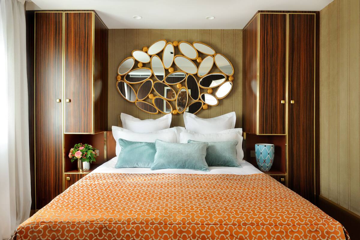 A hotel room with a large bed, a decorative mirror above the bed, and wooden paneling on the walls.