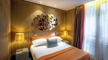 Una camera d'hotel con un letto grande, uno specchio decorativo, due lampade da comodino e vista all'esterno tramite tende leggere.