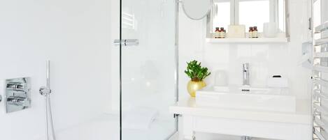 Un baño moderno con cabina de ducha de vidrio, un lavamanos blanco con espejo arriba y un perchero.