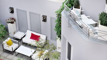 Una terrazza esterna con mobili bianchi, un cuscino rosso e un divano bianco.