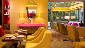 A modern dining area with yellow chairs, a pink table, and a large mirror above a pink console. - Hôtel Baume (Paris)