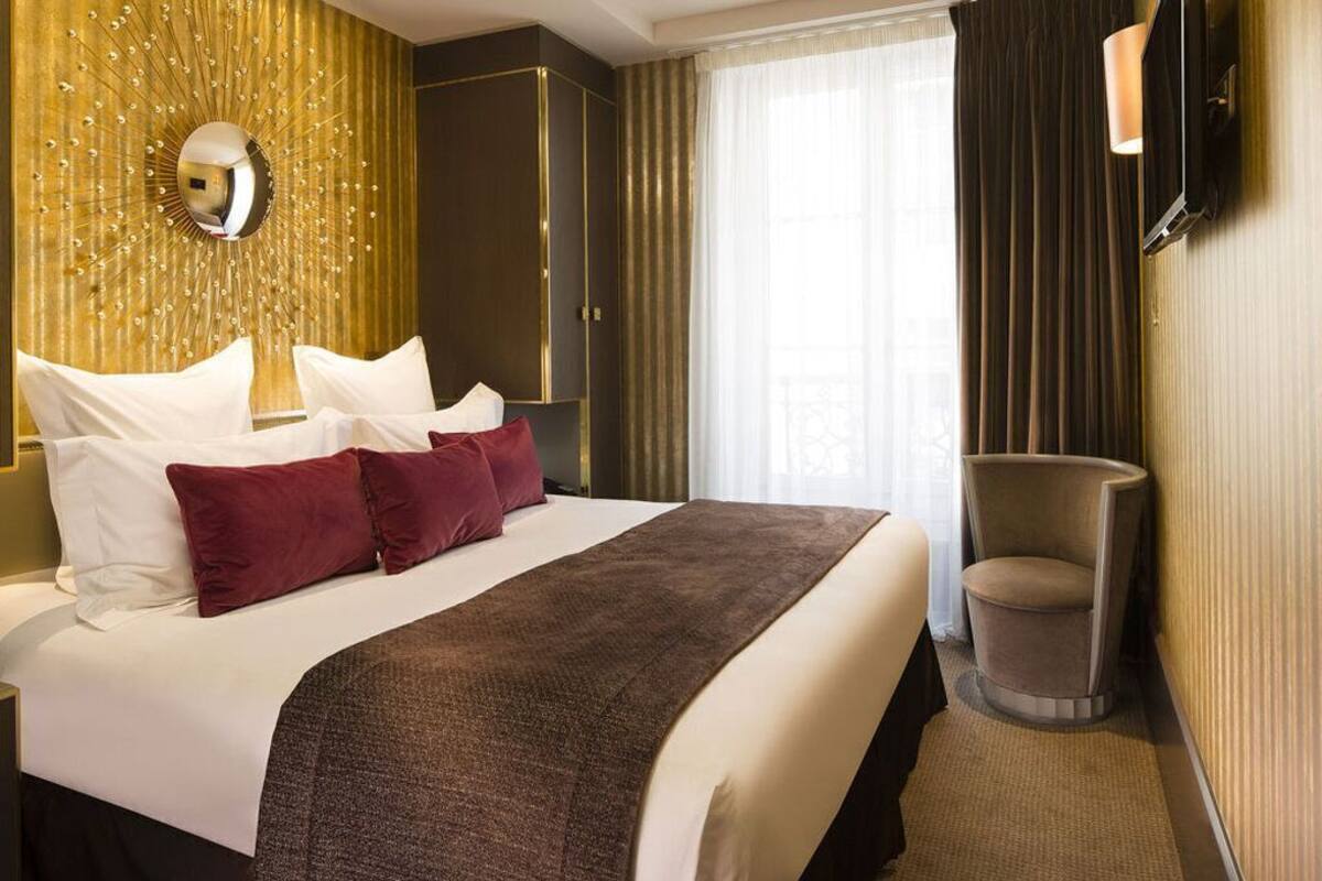 A hotel room with a large bed, a mirror, a television, and a chair.