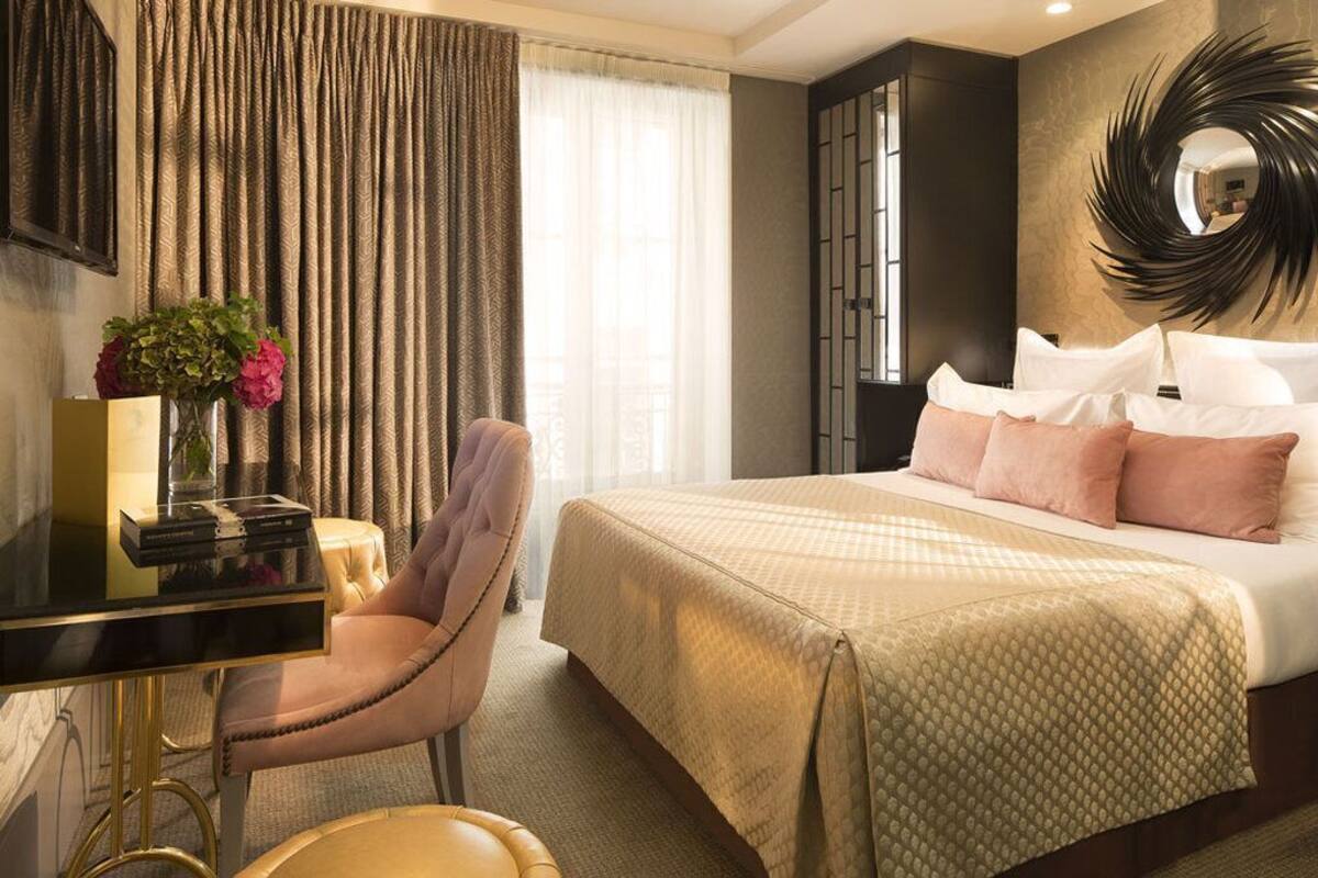 A hotel room with a bed, a desk, a chair, a mirror, and a window with curtains.