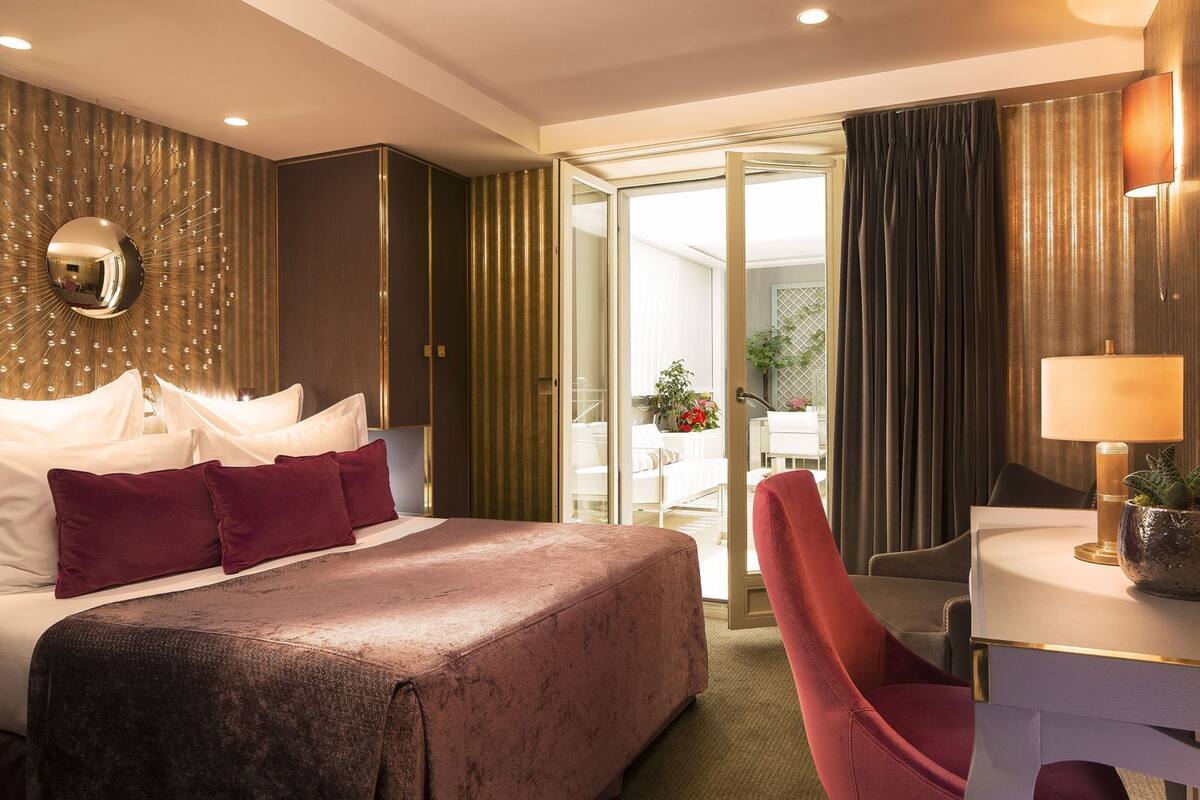 A hotel room with a large bed, a desk with a lamp, a chair, and a view of the outside.