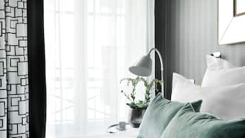 A modern bedroom with a bed, a bedside table with a lamp, a potted plant, and sheer curtains.