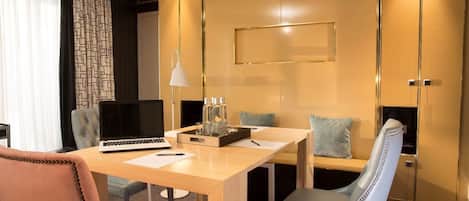 A hotel room with a wooden desk, two chairs, a laptop, a lamp, and a minibar.