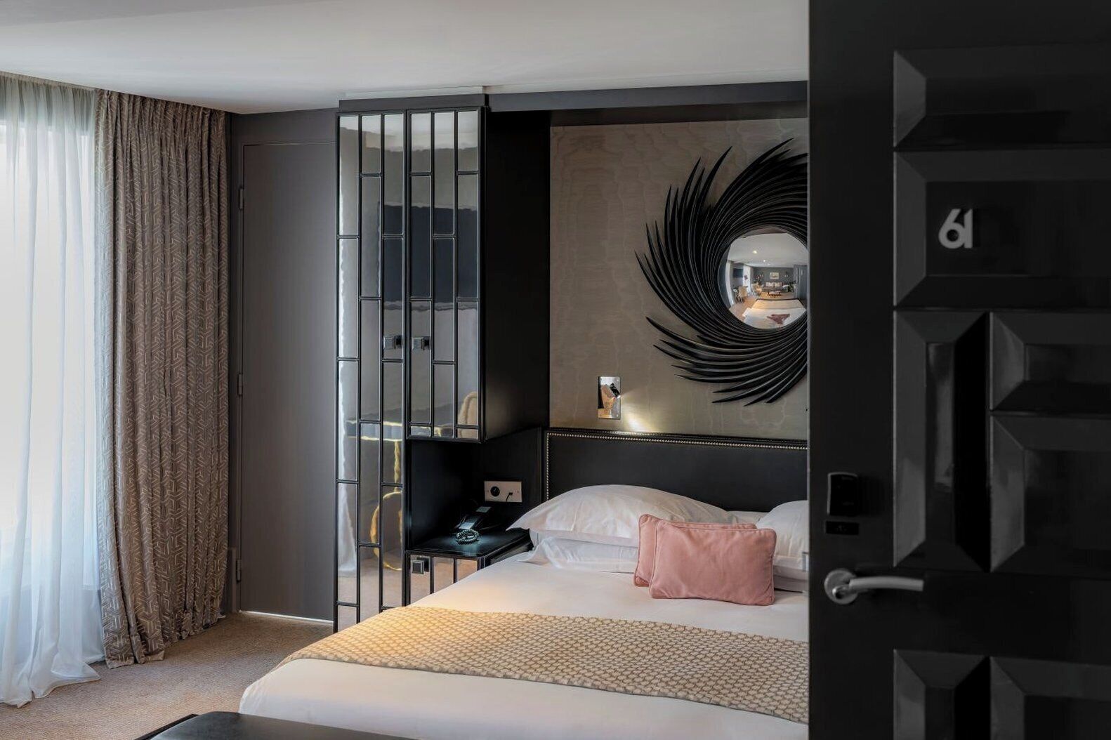 Quarto de hotel moderno com uma cama, uma mesinha de cabeceira, um espelho e uma porta com um número.