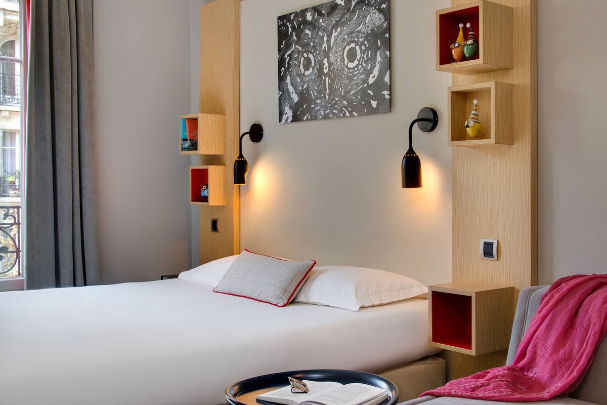 Een hotelkamer met een bed, nachtkastjes, een aan de muur hangend kunstwerk en decoratieve objecten.