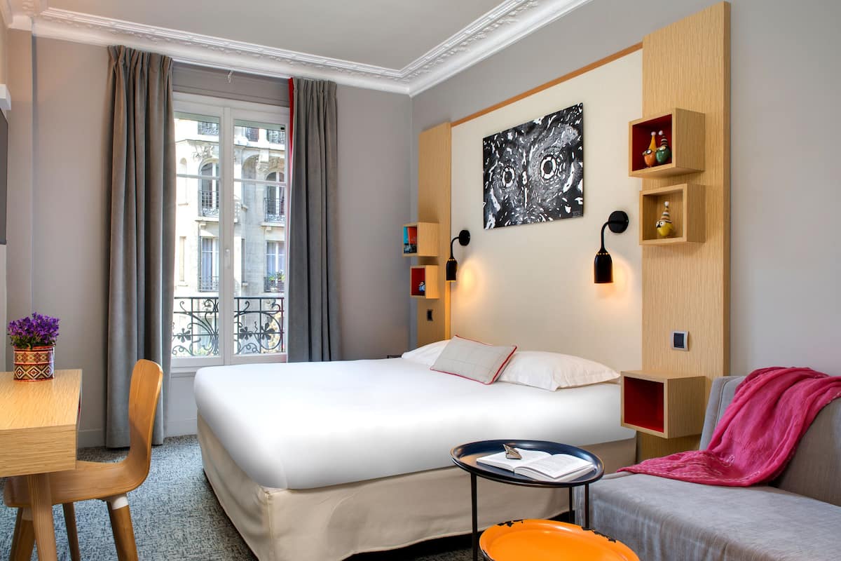 Een hotelkamer met een bed, bureau, stoel, een klein tafeltje, een bank en een raam met gordijnen.