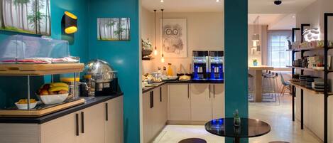 A modern kitchen with teal walls, wooden cabinets, and a central island with stools. There are various kitchen appliances and a dining area visible.