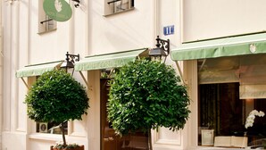 Un hôtel avec un auvent vert, une enseigne ornée d’un symbole de couronne et deux plantes suspendues.