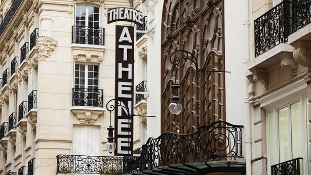 Un bâtiment sur lequel on peut lire l’inscription « THÉÂTRE ATHÈNE », et qui est doté de balcons en fer forgé noir richement décorés.
