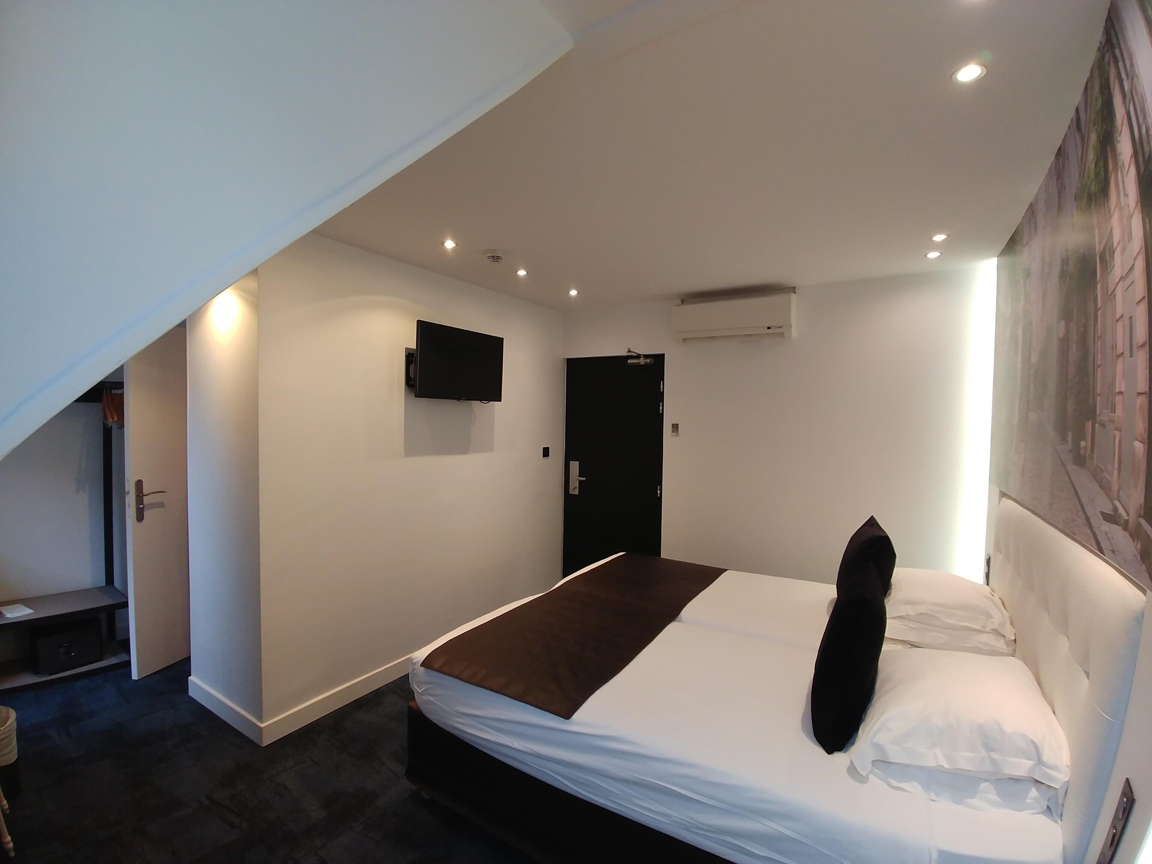 Ein modernes Hotelzimmer mit einem Bett, einem flachbildfernseher an der Wand, einer Klimaanlage und einer Tür.