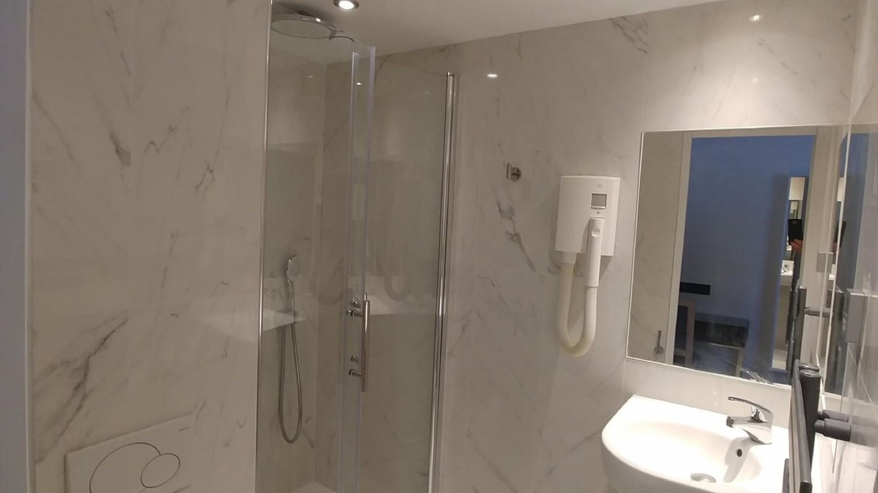 A modern bathroom with a glass-enclosed shower, a white sink, and a mirror.