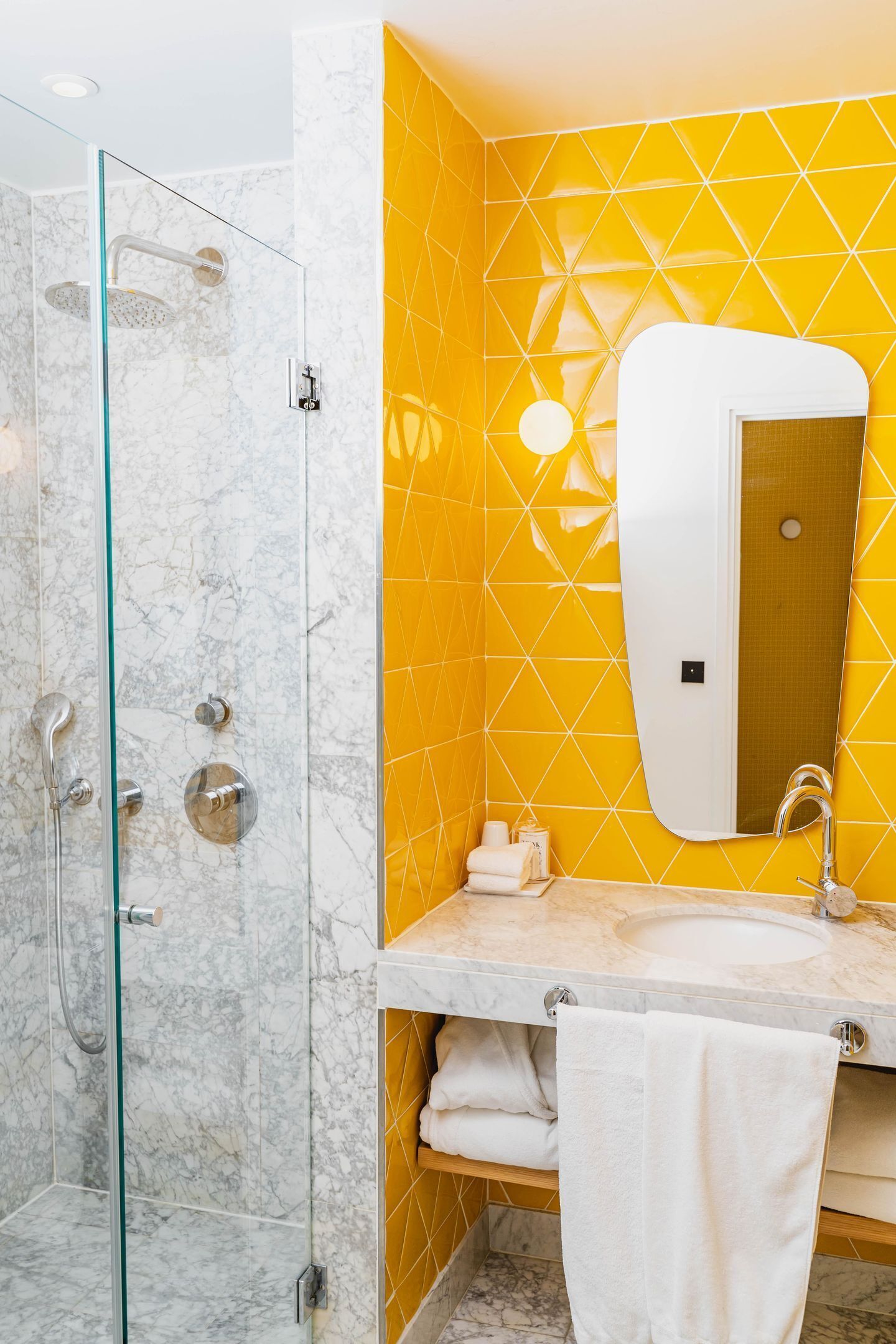 A bathroom with a glass shower enclosure, a marble sink, and a yellow geometric wall pattern.