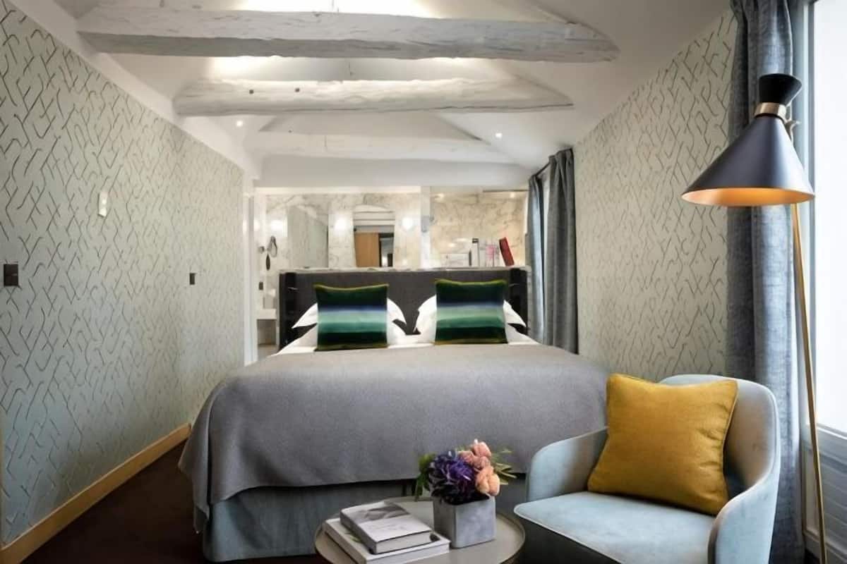 A hotel room with a bed, a chair, a lamp, and a small table with books and flowers.