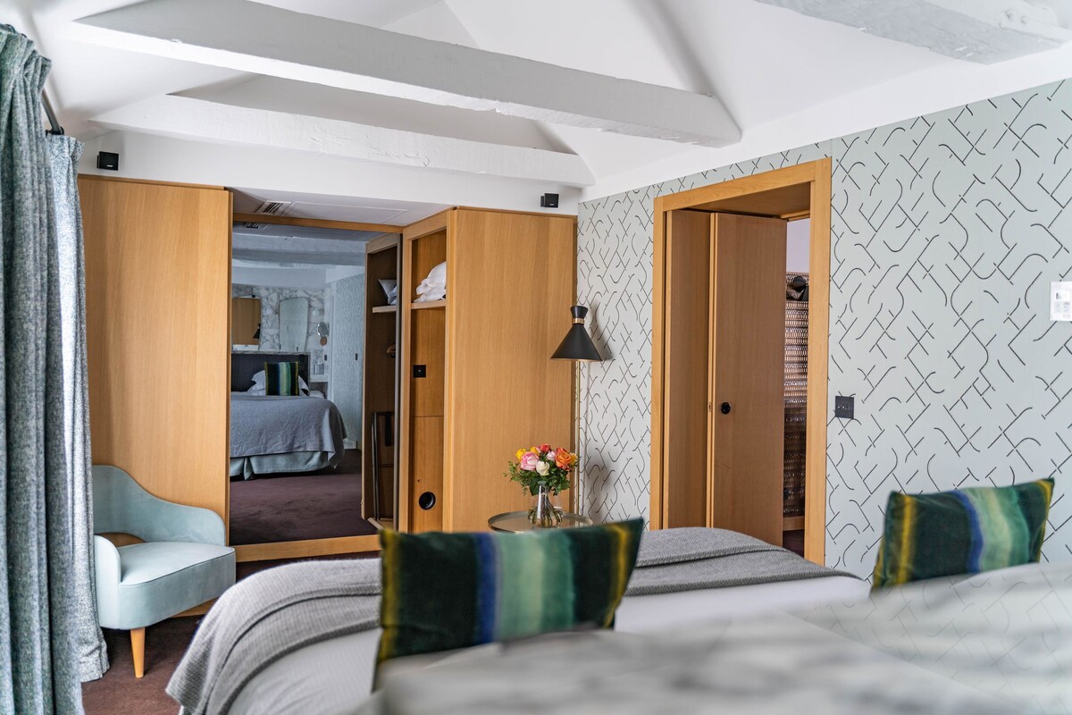 A hotel room with a bed, a small table with a vase of flowers, a chair, and a wardrobe.