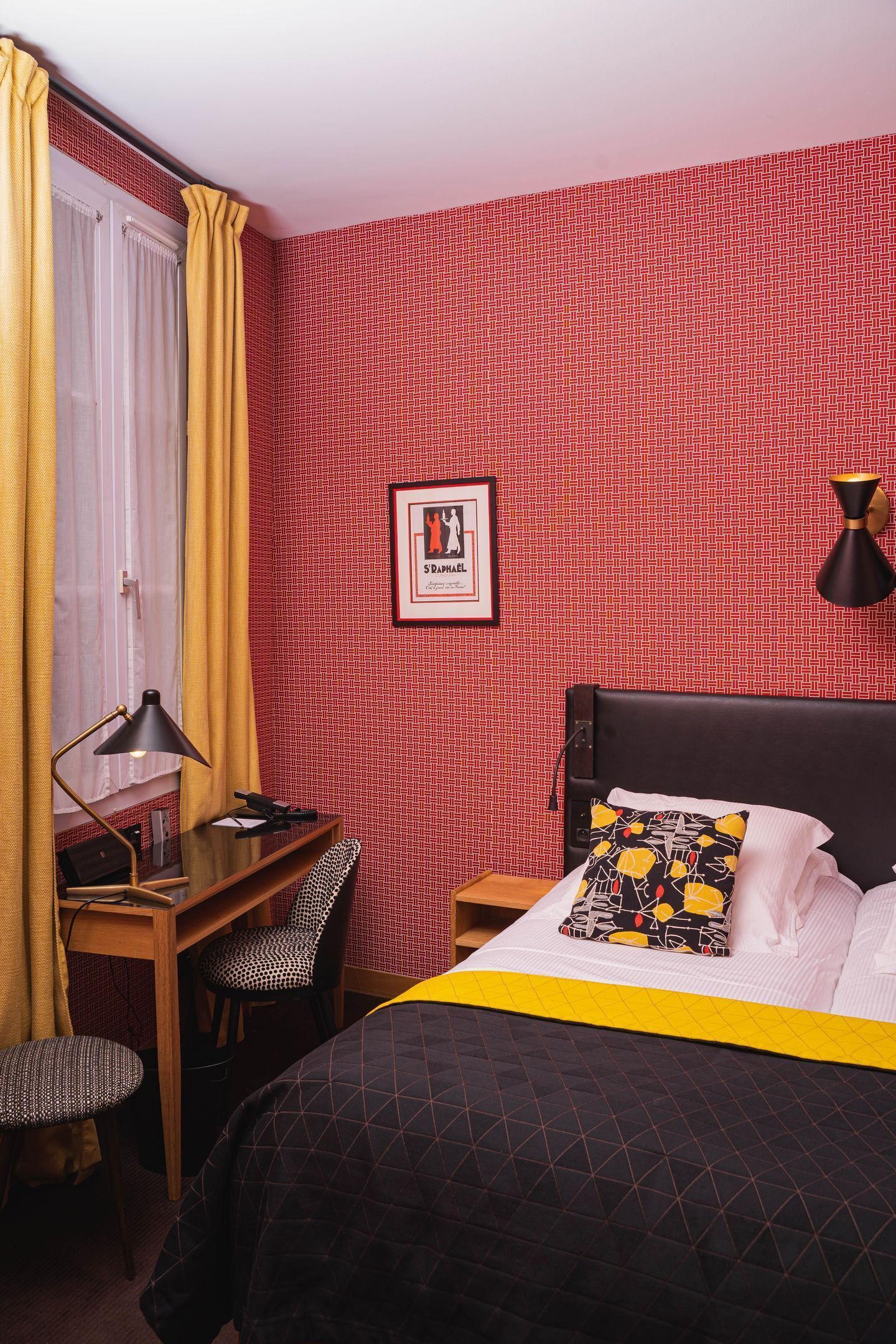Ein Hotelzimmer mit Bett, Schreibtisch, Stuhl, Lampe und einem gerahmten Bild an der Wand.