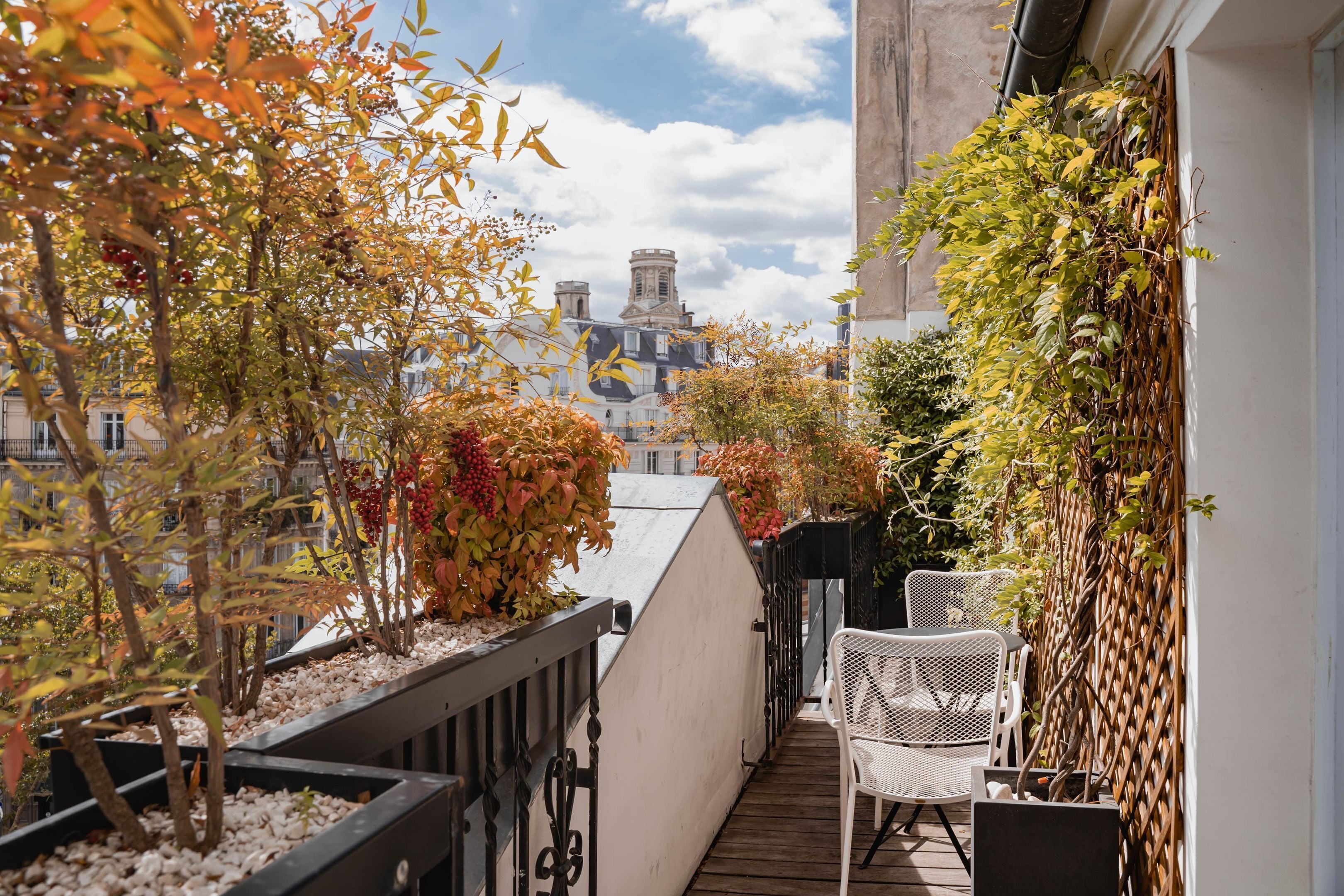 A balcony with a view of buildings, white wicker chairs, and plants.