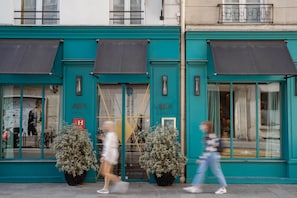 A hotel facade with teal exterior, large windows, and two potted plants. - Hôtel Artus (Paris)