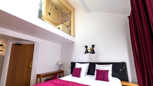 A bedroom with a bed, a desk, a lamp, a red curtain, and a skylight. - Hôtel Artus (Paris)