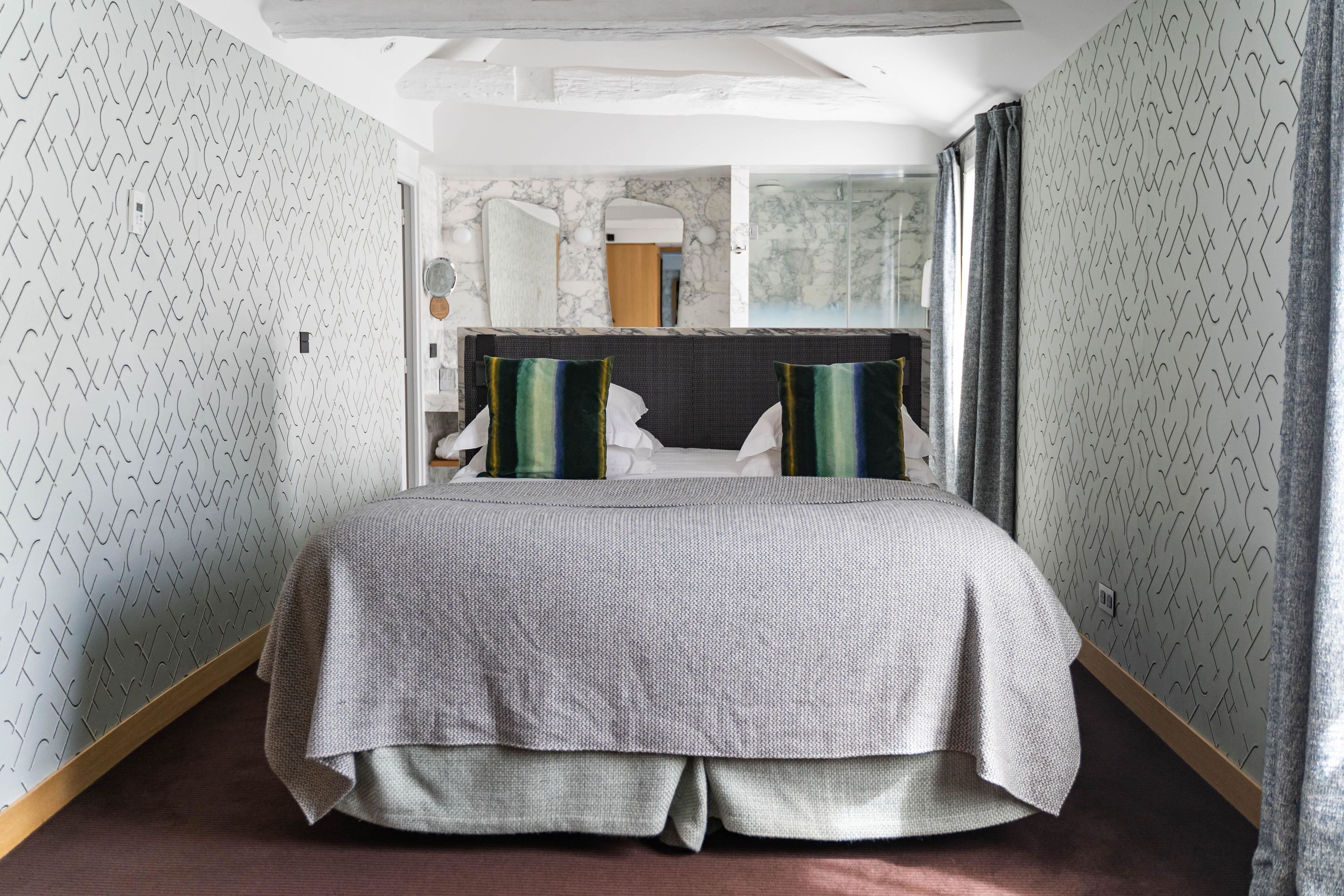 A modern hotel room with a large bed, a marble wall, and a view of the city.