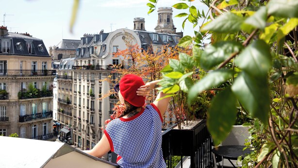A balcony with a view of Parisian buildings, a red hat, and a checkered shirt. - Hôtel Artus (Paris)